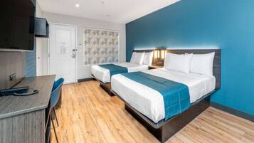A hotel room with two beds, a desk, and a TV.