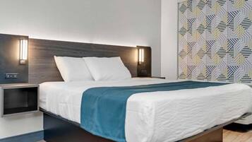 A modern hotel room with a large bed, a nightstand, a wall-mounted light, and a patterned wall.