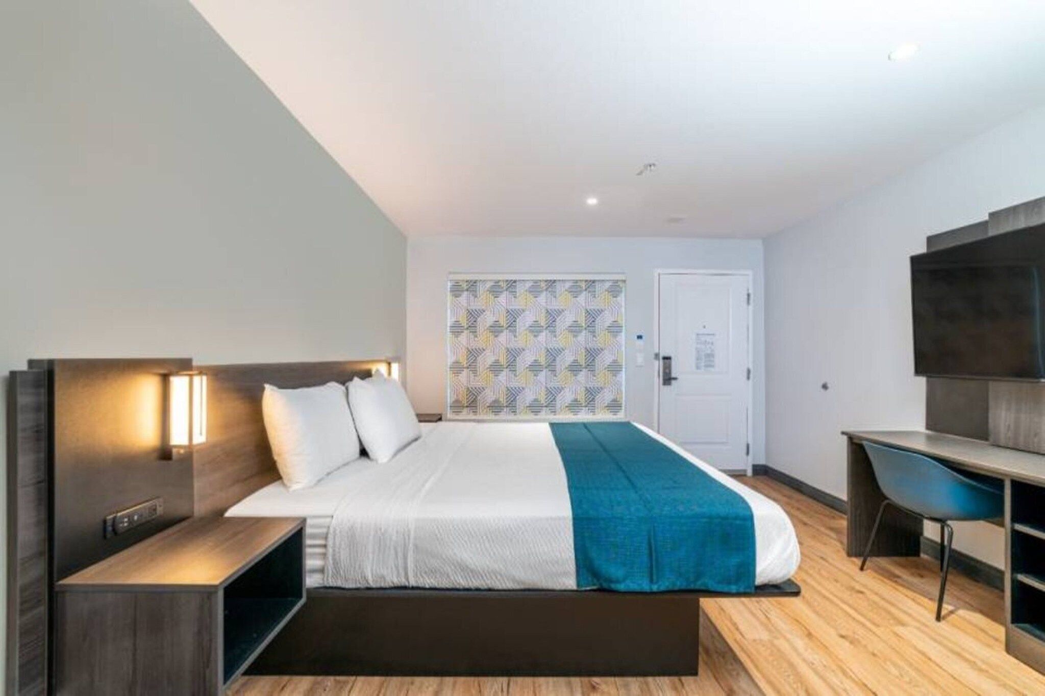 A modern hotel room with a bed, bedside tables, a desk, and a TV.