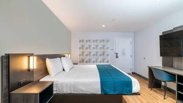 A modern hotel room with a bed, bedside tables, a desk, and a TV.