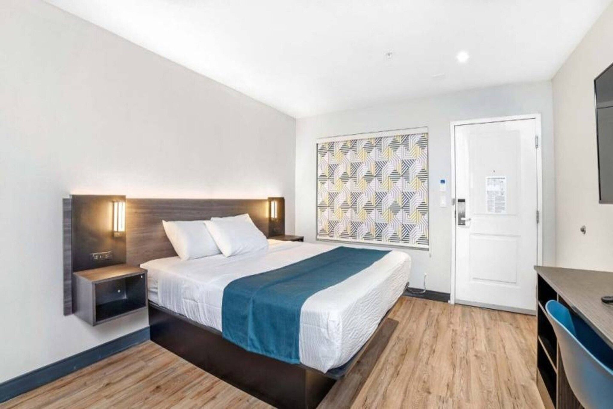 Ein Hotelzimmer mit Bett, Nachttisch, Wandleuchte und einer Tür.