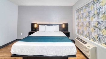 Ein modernes Hotelzimmer mit einem großen Bett, einer Kopfteilbeleuchtung, einer Wand mit Muster und einer fest installierten Klimaanlage.