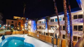 A hotel with a swimming pool, multiple balconies, and a well-lit exterior.