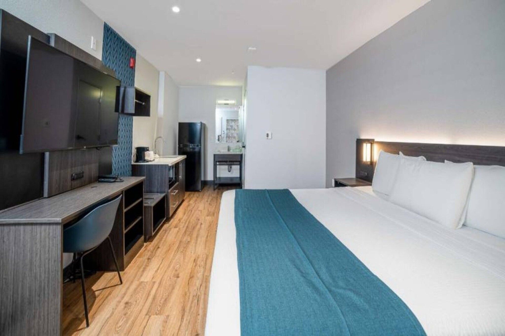 A hotel room with a bed, a desk, a TV, and a kitchenette.