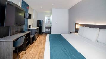 A hotel room with a bed, a desk, a TV, and a kitchenette.