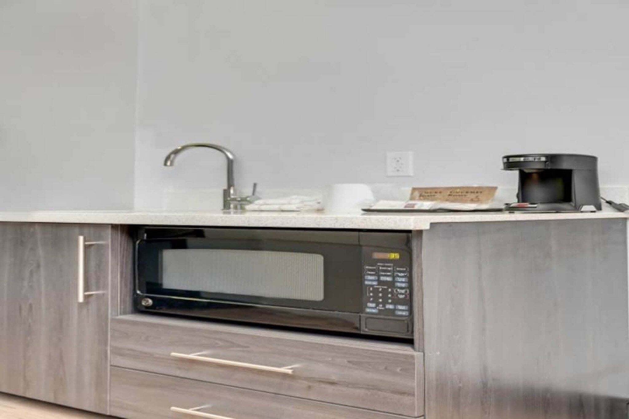 A kitchen with a built-in microwave, a coffee maker, and a sink.