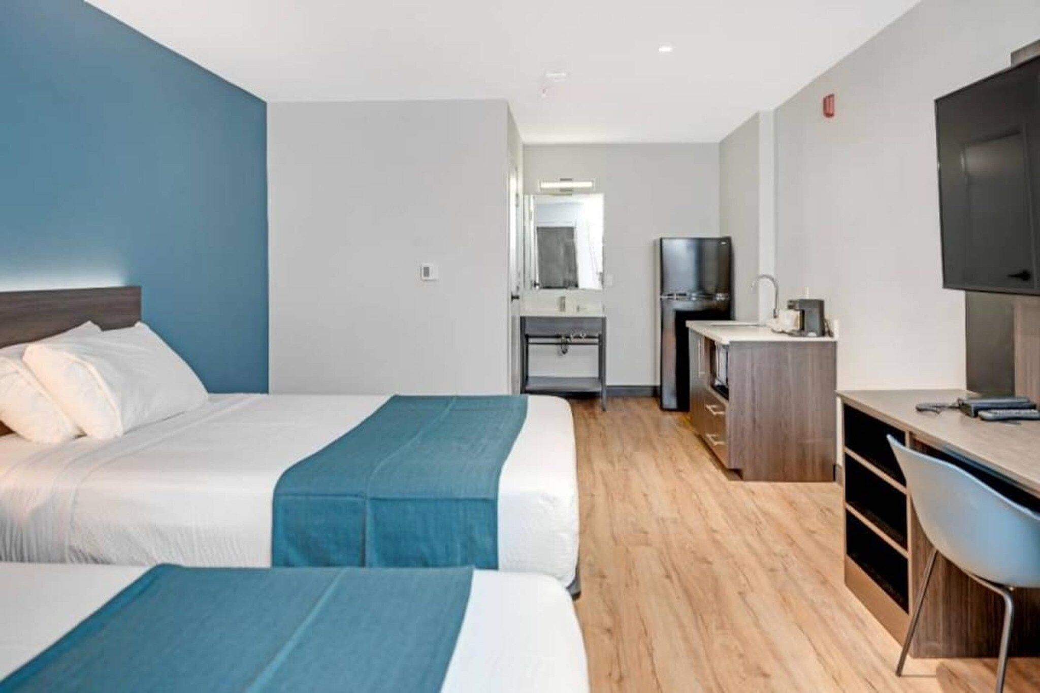 A hotel room with two beds, a desk, a television, and a kitchenette.