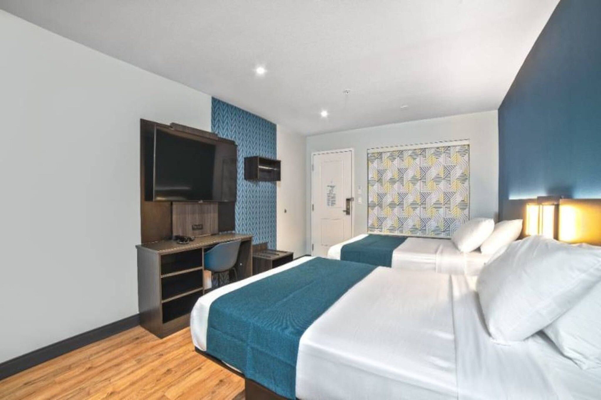 A hotel room with two beds, a desk, a television, and a patterned wall.