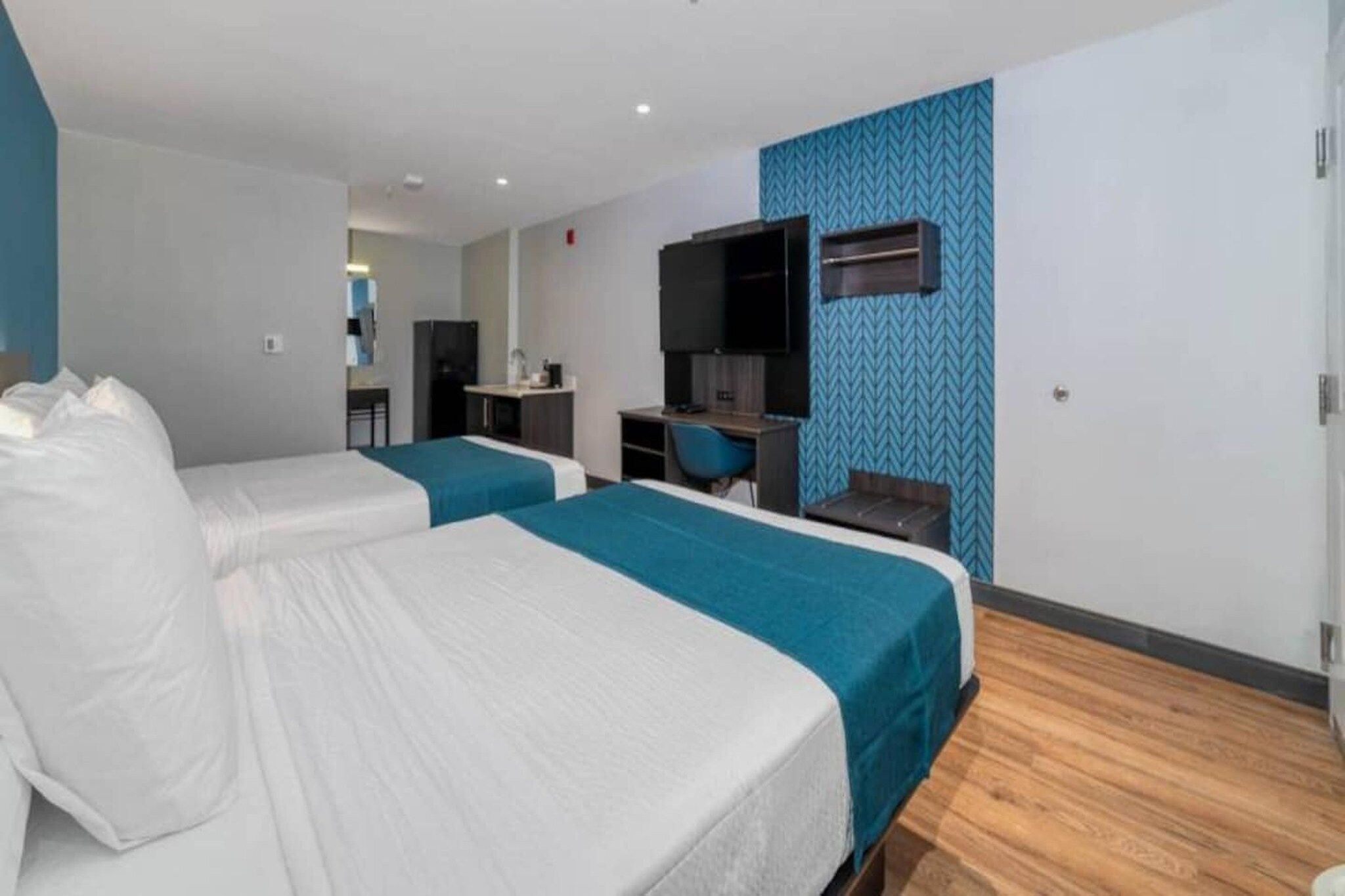 Ein Hotelzimmer mit zwei Betten, einem Schreibtisch, einem Stuhl, einem Fernseher und einer Küchenzeile.