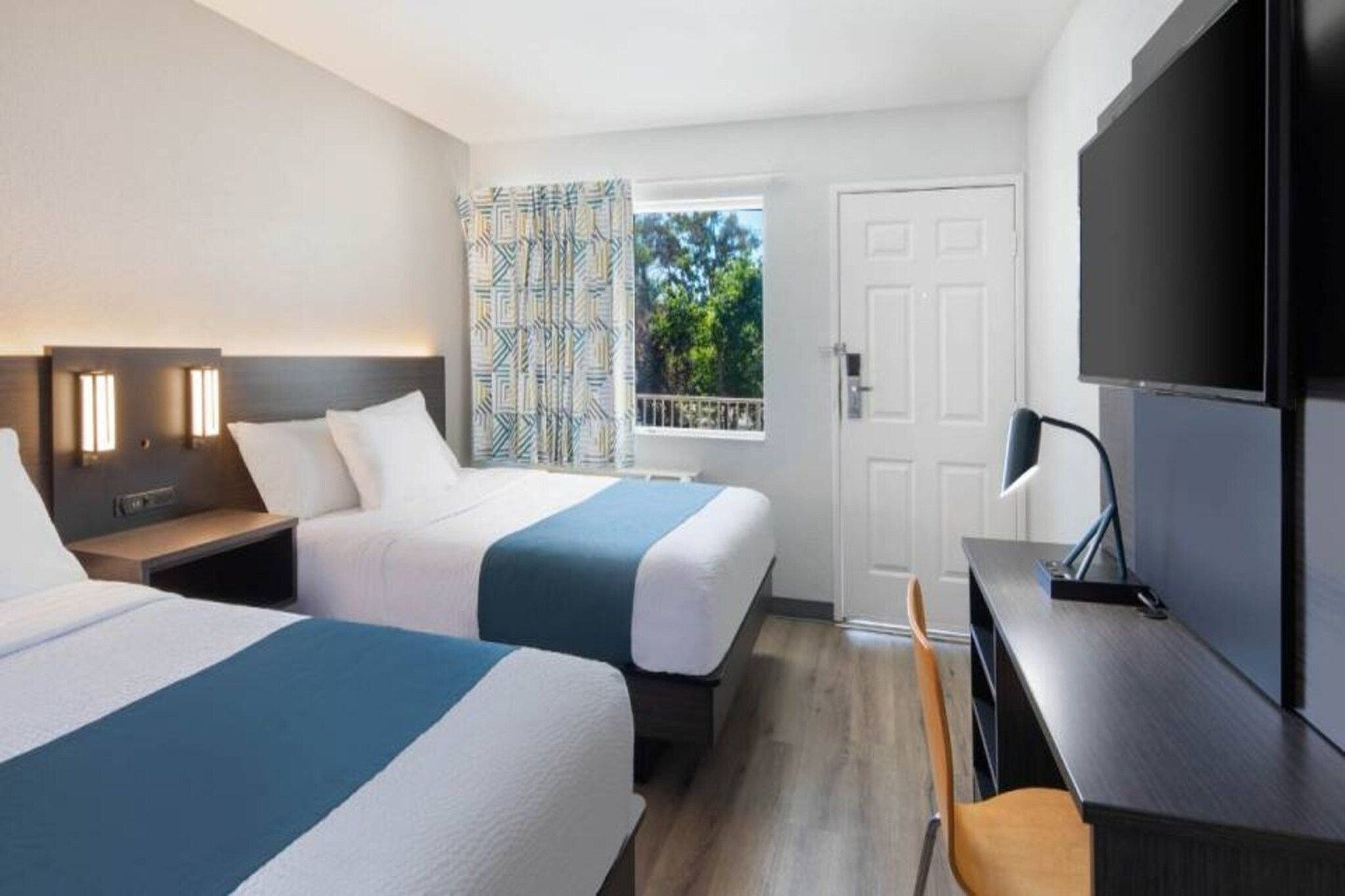 Une chambre d’hôtel avec deux lits, un bureau, une chaise, une télévision et une fenêtre avec des rideaux.