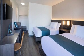 Habitación de hotel con dos camas, un escritorio, una silla y un televisor.