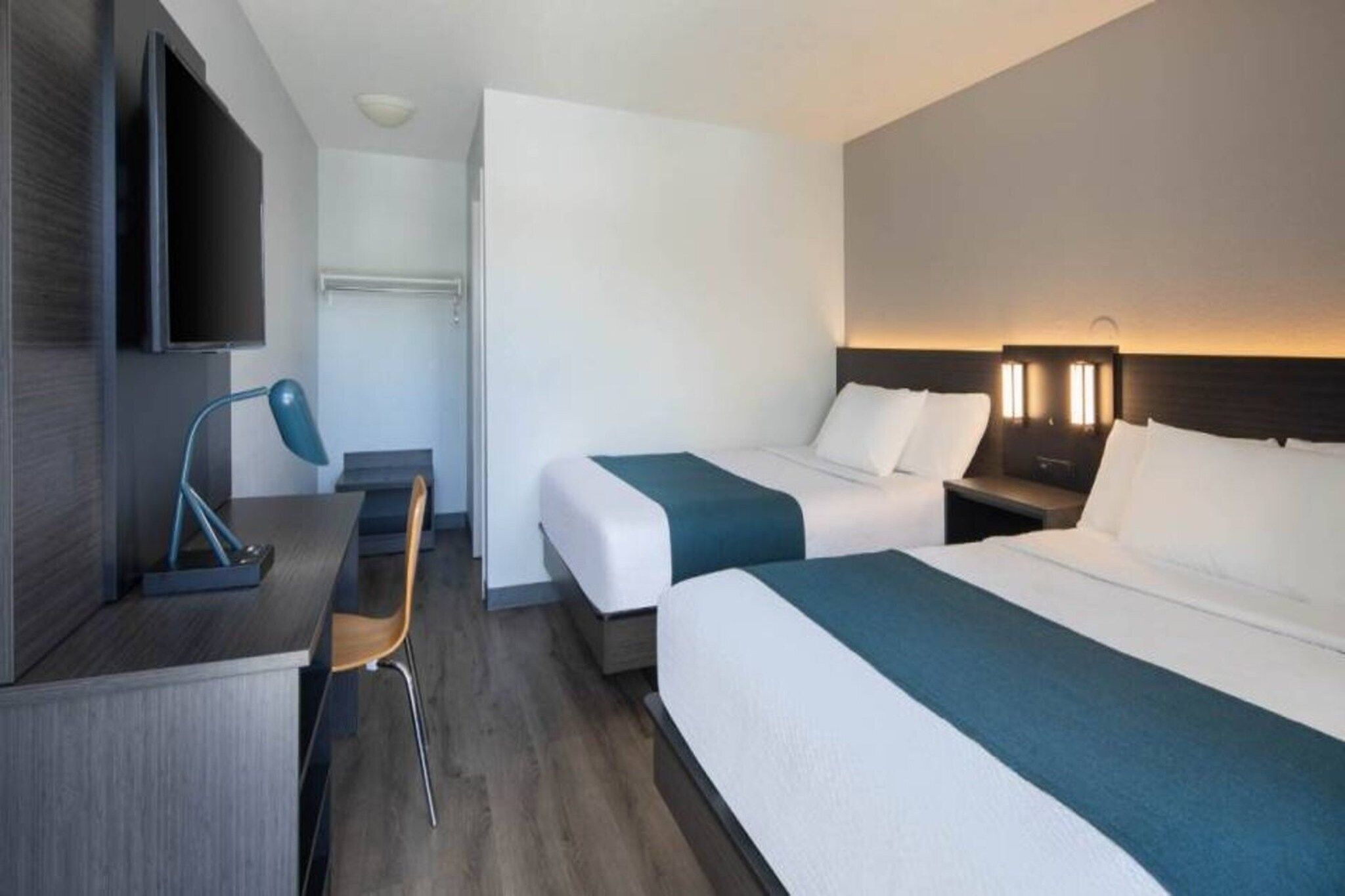 A hotel room with two beds, a desk, a chair, and a television.
