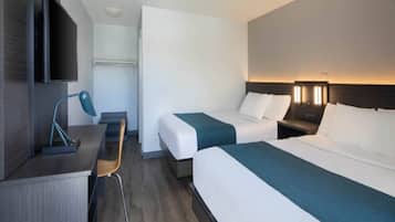 A hotel room with two beds, a desk, a chair, and a television.