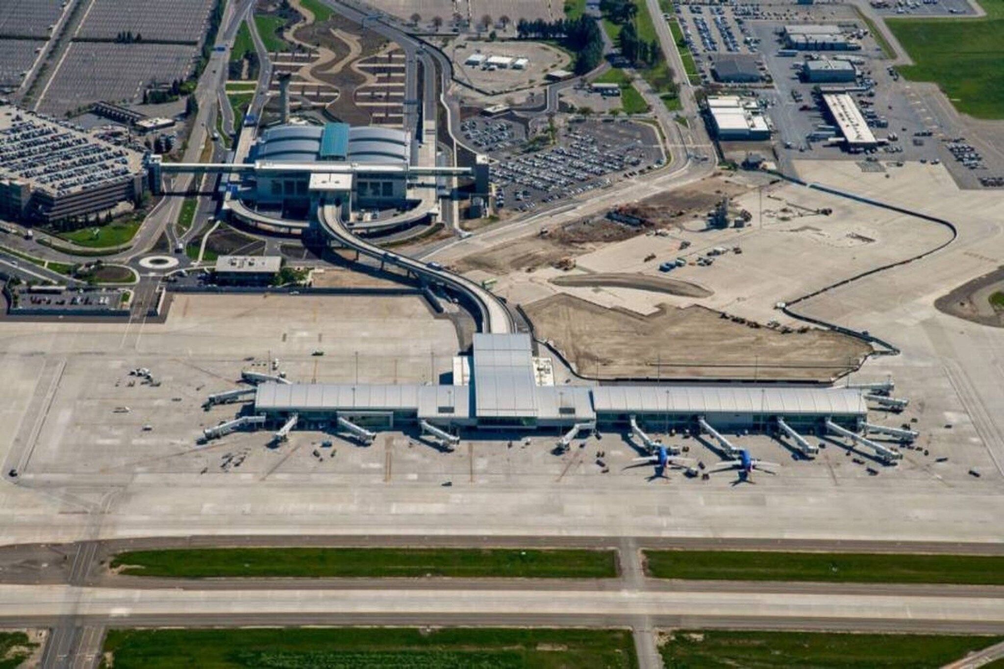 An airport terminal with multiple jet bridges, a central building, and a parking area.