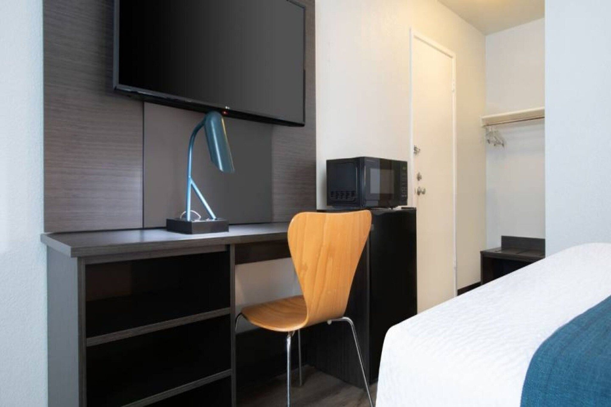 A hotel room with a bed, a desk with a chair, a television, and a microwave.