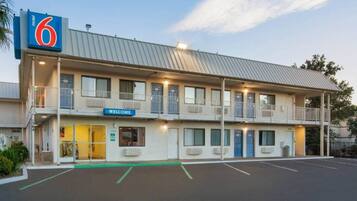Un motel con un letrero con el número '6', un letrero de 'Bienvenido' y un estacionamiento.