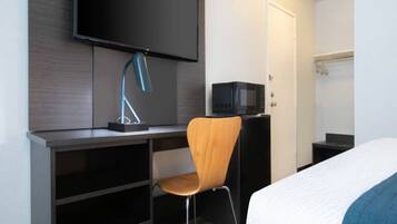 A hotel room with a bed, a desk with a chair, a television, and a microwave.