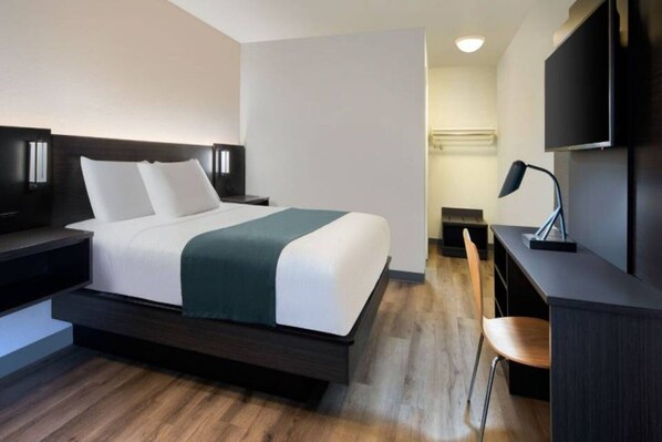 A modern hotel room with a bed, bedside tables, a desk, a chair, and a TV.