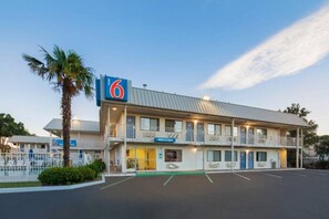 Un motel con un letrero con el número '6', un letrero de 'Bienvenido' y un estacionamiento.