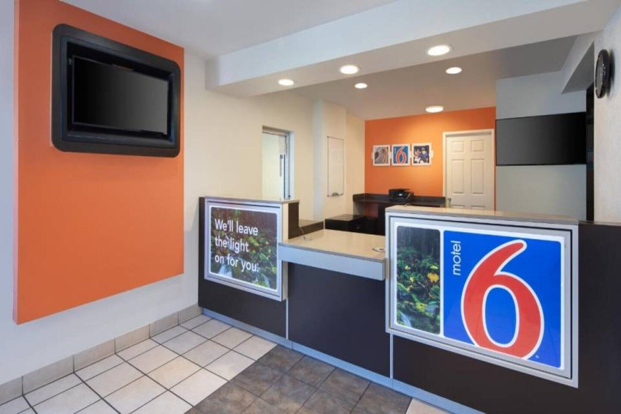 A reception area with a counter, a television mounted on the wall, and a sign indicating the motel number.