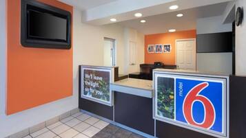 A reception area with a counter, a television mounted on the wall, and a sign indicating the motel number.
