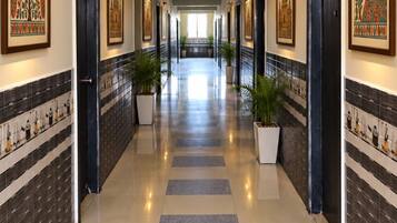 Un pasillo de hotel con piso de estampado de cuadros, obras de arte enmarcadas en las paredes y plantas en macetas.