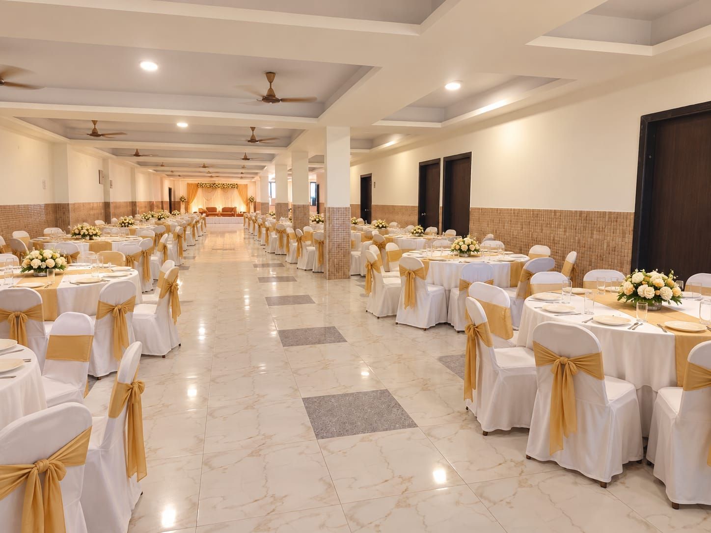Un salón de banquetes con filas de mesas dispuestas para comer, sillas con cintas doradas y un escenario al fondo.