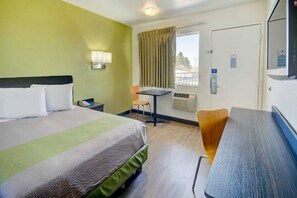 Ein Hotelzimmer mit Bett, Schreibtisch, Stuhl, einem Fenster mit Vorhängen und einem Fernseher.