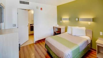 A hotel room with a bed, a desk, a chair, and a small table.