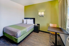 Ein Hotelzimmer mit Bett, Nachttisch, Lampe, Stuhl und kleinem Tisch.