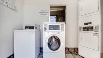 A laundry area with a front-loading washer and dryer, a refrigerator, and a sign indicating the hotel is not responsible for unattended items.