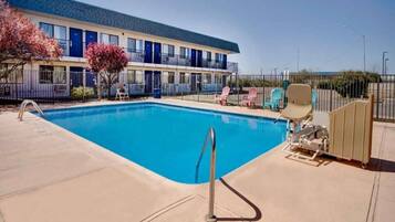 A swimming pool with a metal ladder, surrounded by lounge chairs and a fence.