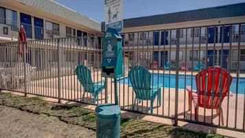 A fenced pool area with chairs and a trash can, a pet waste sign, and a building with multiple windows and doors.