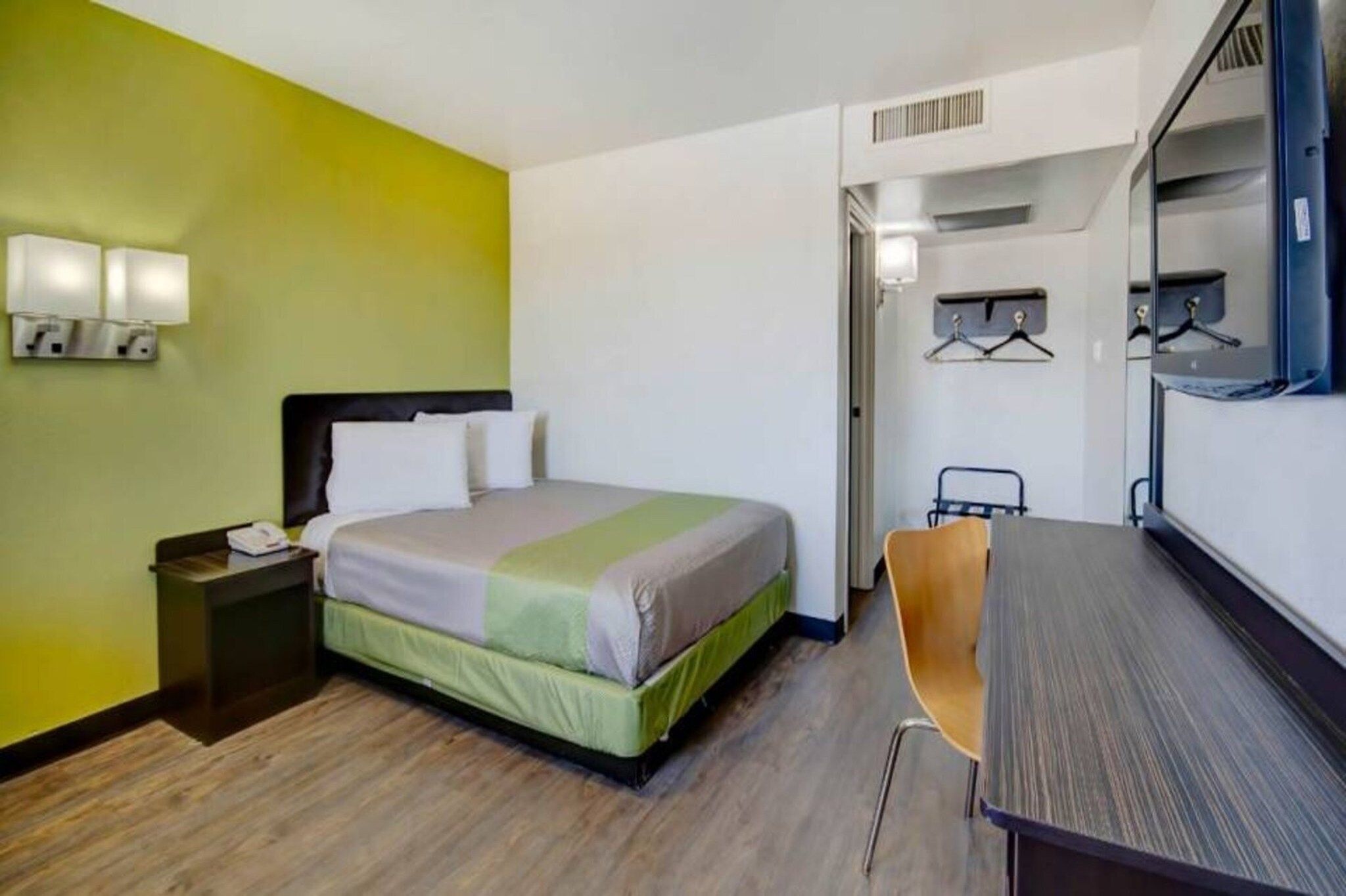 A hotel room with a bed, bedside table, chair, and a desk with a mirror.