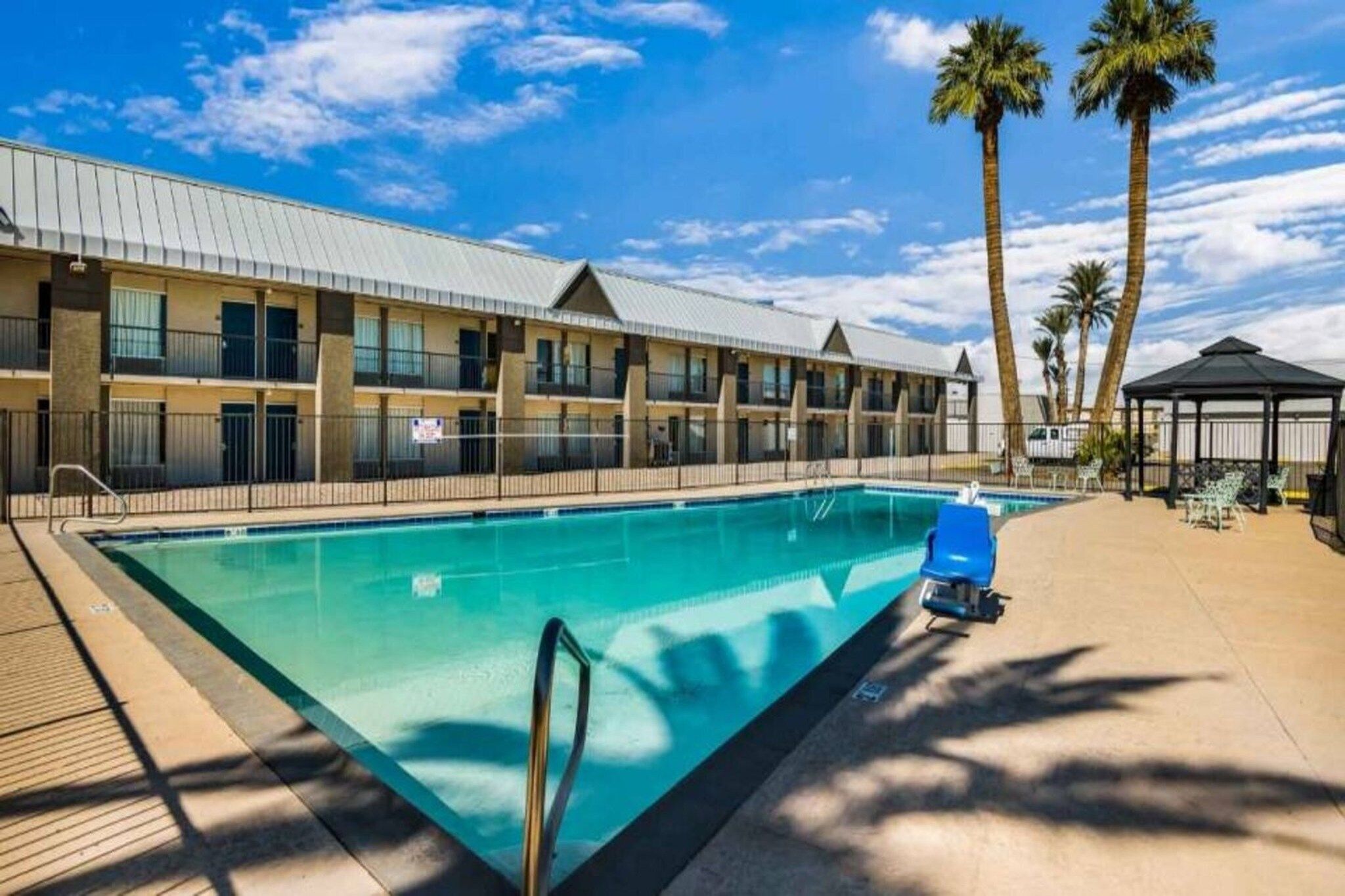 A hotel with a swimming pool, palm trees, and a covered seating area.