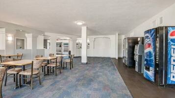 A hotel lobby with a carpeted floor, seating area with tables and chairs, vending machines, and a large pillar.