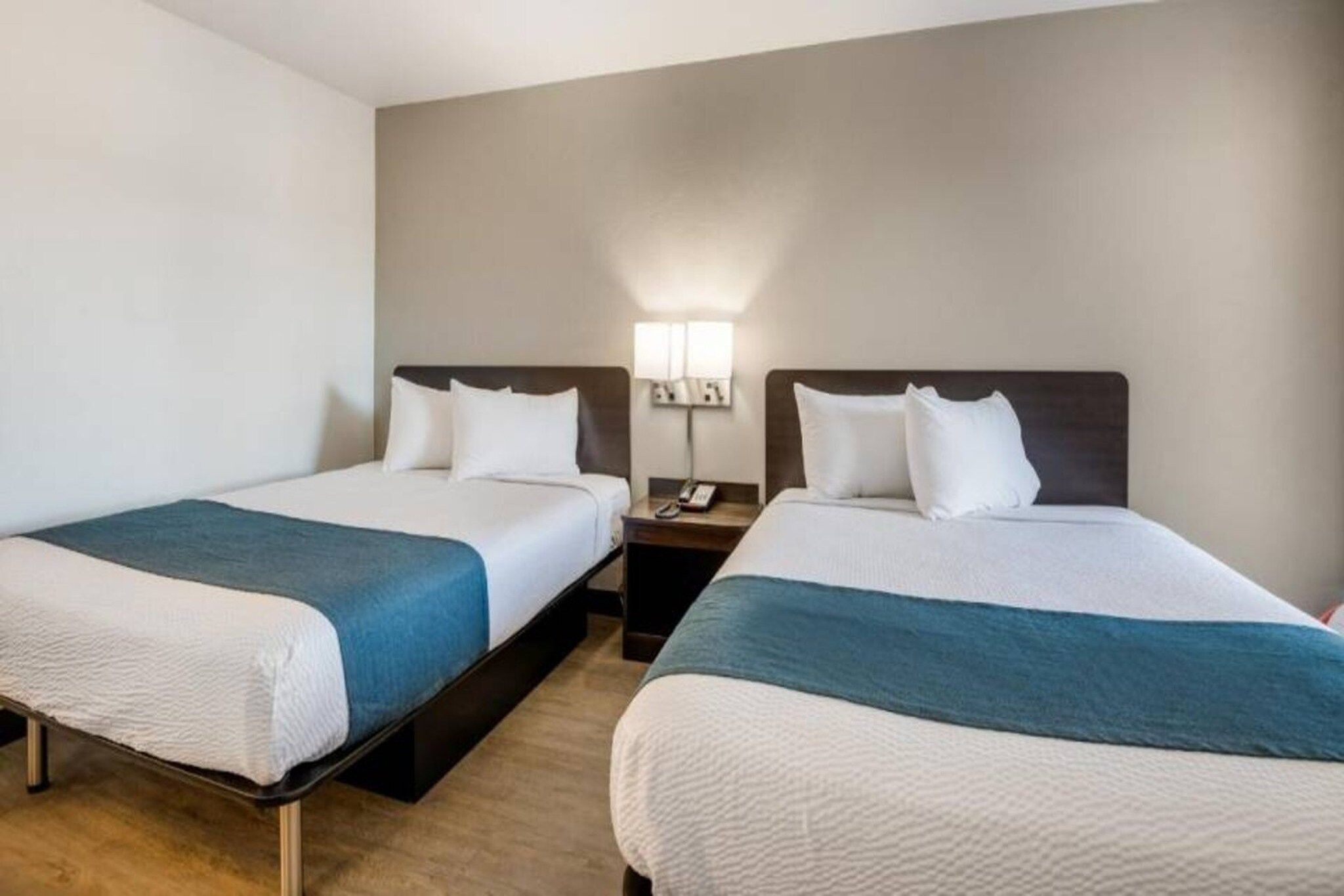 A hotel room with two beds, a nightstand, and a wall-mounted lamp.