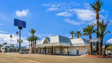 A motel with a large blue sign, a parking lot, and palm trees.