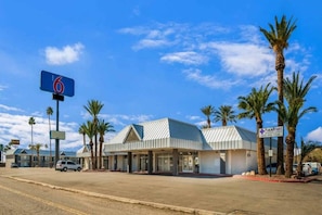 Un motel con un gran letrero azul, un estacionamiento y palmeras.