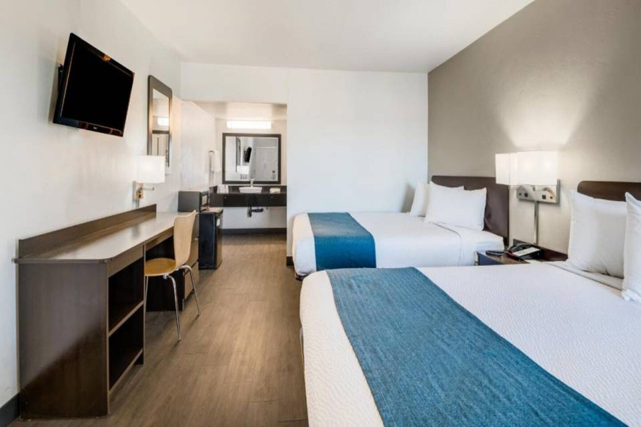 A hotel room with two beds, a desk, a chair, a television, and a mirror.