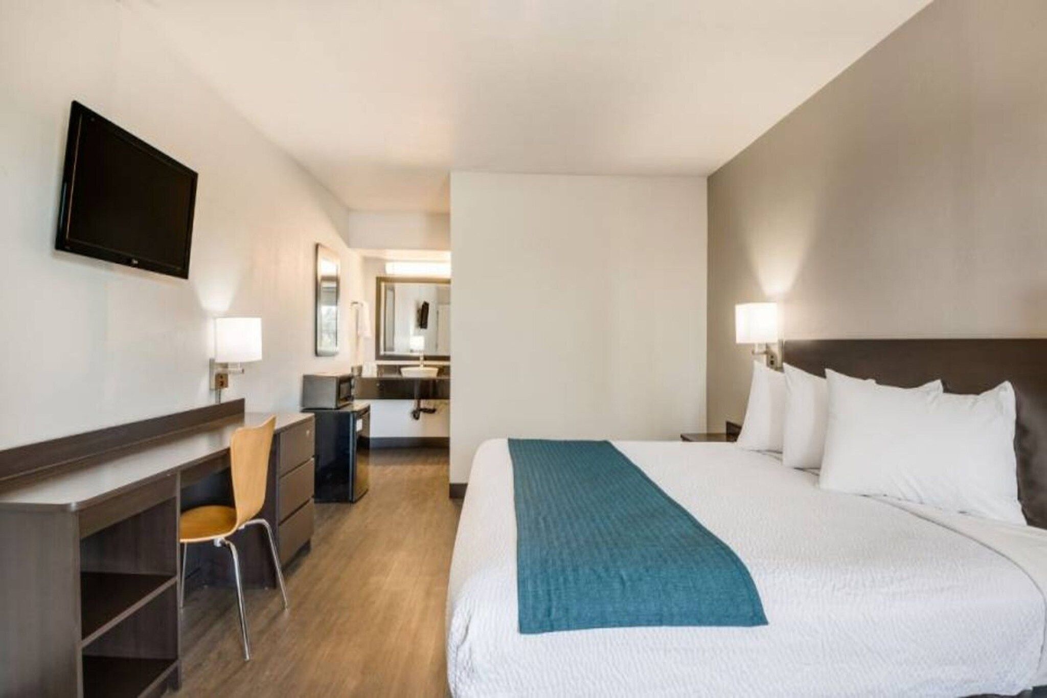 Ein Hotelzimmer mit Bett, Schreibtisch, Stuhl, Fernseher und Spiegel.