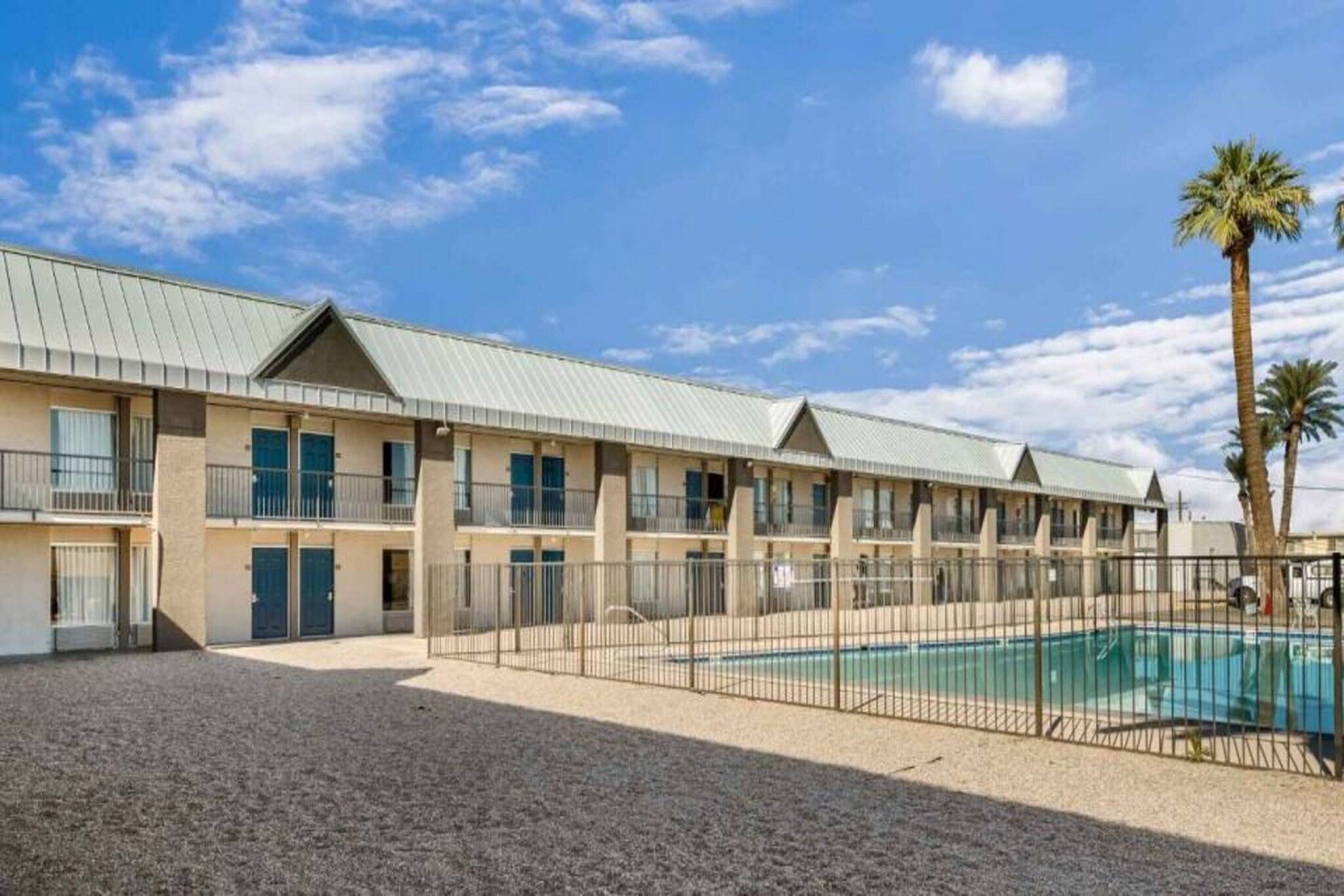 Ein Motel mit mehreren Zimmern, einem Schwimmbecken und einem Kieshof.
