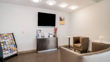 A reception area with a flat-screen TV mounted on the wall, a magazine rack, a small table with a vase, and a cushioned seating area.
