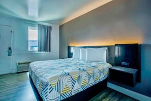 A modern hotel room with a large bed, a flat-screen TV, and a window with curtains.