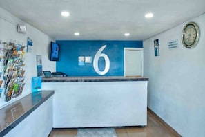 A reception desk with a prominent number '6' on the wall, a clock, and a magazine rack.