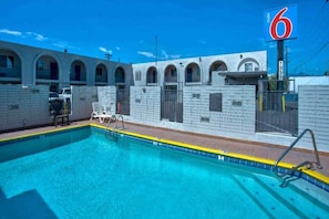 Une piscine à l’eau d’un bleu cristallin, entourée d’un mur blanc orné de fenêtres en arc de cercle, et un panneau indiquant le chiffre 6.