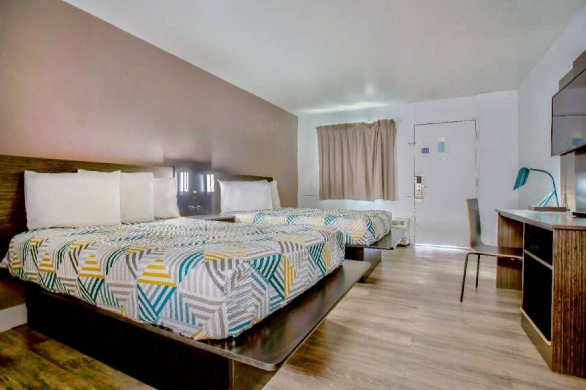 A hotel room with two beds, a desk, a chair, and a television.