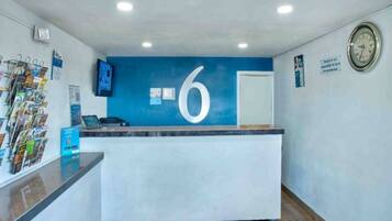 A reception desk with a prominent number '6' on the wall, a clock, and a magazine rack.
