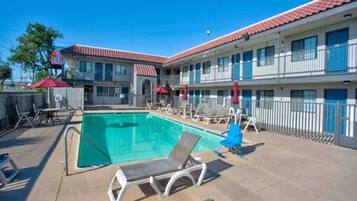 A hotel with a swimming pool, outdoor seating, and a red and blue color scheme.