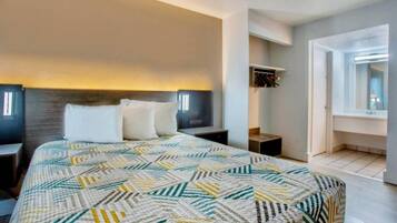 Un dormitorio con una cama grande, una mesita de noche, un estante en la pared y una puerta que da a otra habitación.